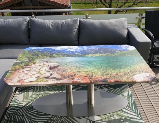 Tisch-Glasplatte mit Digitaldruck, hier ein Blick vom Ufer auf einen See mit klarem Wasser in den Bergen.